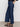 A person stands against a plain background wearing Sanctuary Clothing's league crop plot twist top, paired with wide-leg dark blue jeans and black sandals, with one hand in their back pocket.