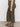 A person wears Sanctuary Clothing’s league crop fatigue extended sizing olive green high-waisted, straight-leg jeans, a patterned top, and black strappy sandals, standing sideways against a plain white background.