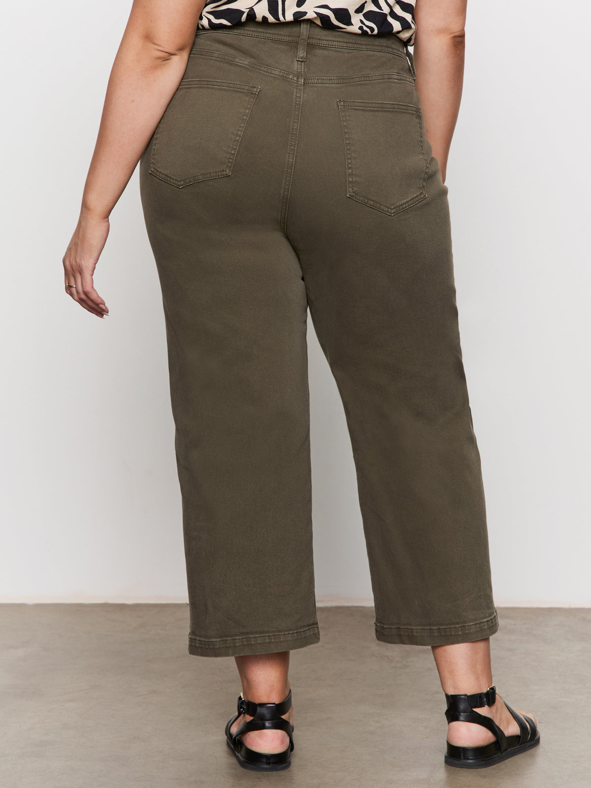 A person wearing Sanctuary Clothing's League Crop Fatigue wide-leg pants in olive green stands with their back to the camera, paired with black sandals, against a light wall and floor.