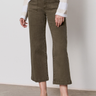 A person wearing Sanctuary Clothing's league crop fatigue pants, paired with a light long-sleeve sweater and white woven flats, stands indoors on a concrete floor against a plain wall.
