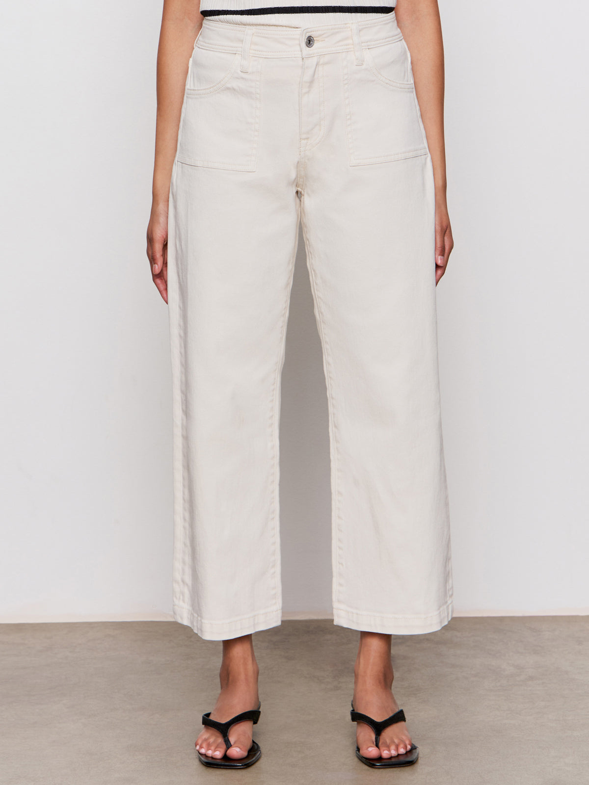 A person is wearing Sanctuary Clothing's league crop light oat wide-leg pants with front patch pockets and black sandals, standing against a plain background.