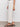 A person models the Sanctuary Clothing league crop light oat jeans, standing sideways in black heeled sandals. Only the lower half of their body is visible against a plain background.