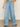 Person wearing Sanctuary Clothing’s Highland Wide Leg Standard Rise Jeans in Sail Away, a black-and-white striped sleeveless top, and black open-toe sandals, standing indoors with one hand in a pocket. Face not visible.