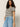 A woman with curly hair wears Sanctuary Clothing's highland wide leg standard rise jeans in sail away, paired with a black and white striped short-sleeve top and stands with one hand in her pocket against a plain background.