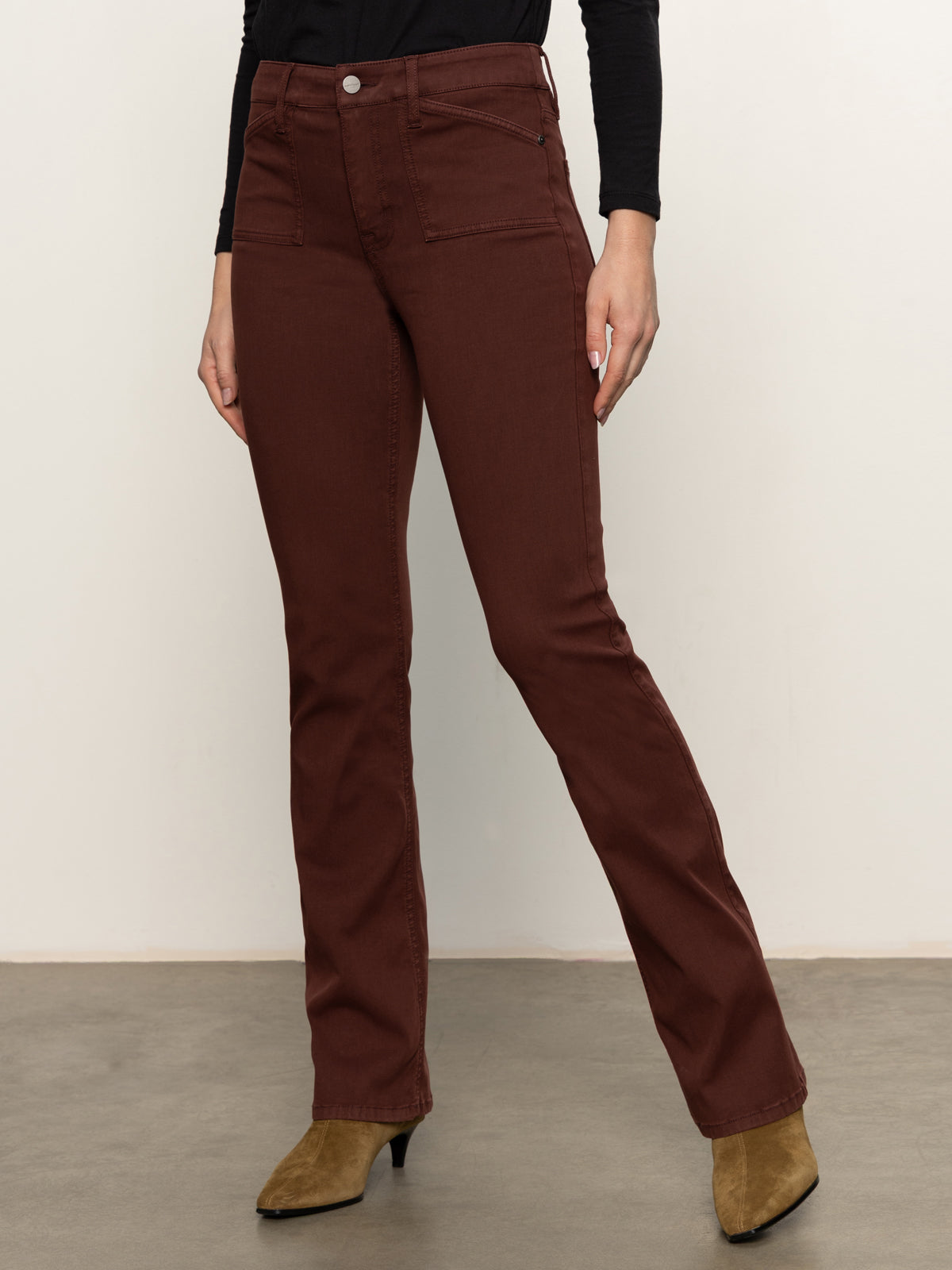 Wearing Sanctuary Clothing's sculpted brook bootcut pant in chicory, paired with a black top and brown pointed-toe heeled boots. The person's head is not visible; they're standing on a gray floor against a plain light wall.