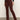 Wearing Sanctuary Clothing's sculpted brook bootcut pant in chicory, paired with a black top and brown pointed-toe heeled boots. The person's head is not visible; they're standing on a gray floor against a plain light wall.