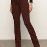Wearing Sanctuary Clothing's sculpted brook bootcut pant in chicory, paired with a black top and brown pointed-toe heeled boots. The person's head is not visible; they're standing on a gray floor against a plain light wall.