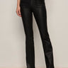 Wearing Sanctuary Clothing's slick brook bootcut pant in black, paired with black pointed-toe boots, a person stands against a neutral background with one hand in their pocket and their upper body mostly out of frame.