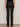 A person faces away from the camera, wearing Sanctuary Clothing's slick brook bootcut pant in black—high-waisted, straight-leg, shiny material—paired with dark heeled shoes against a plain neutral background.