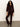 A woman with curly hair wears Sanctuary Clothing„¢s velveteen brook bootcut pant in dark crimson, paired with a matching jacket and brown ankle boots, standing against a plain light background.
