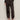 A person wearing Sanctuary Clothing's sahara satin tapered pant in black, paired with a long-sleeved black lace top and black strappy high-heeled sandals, stands against a plain light-colored wall.