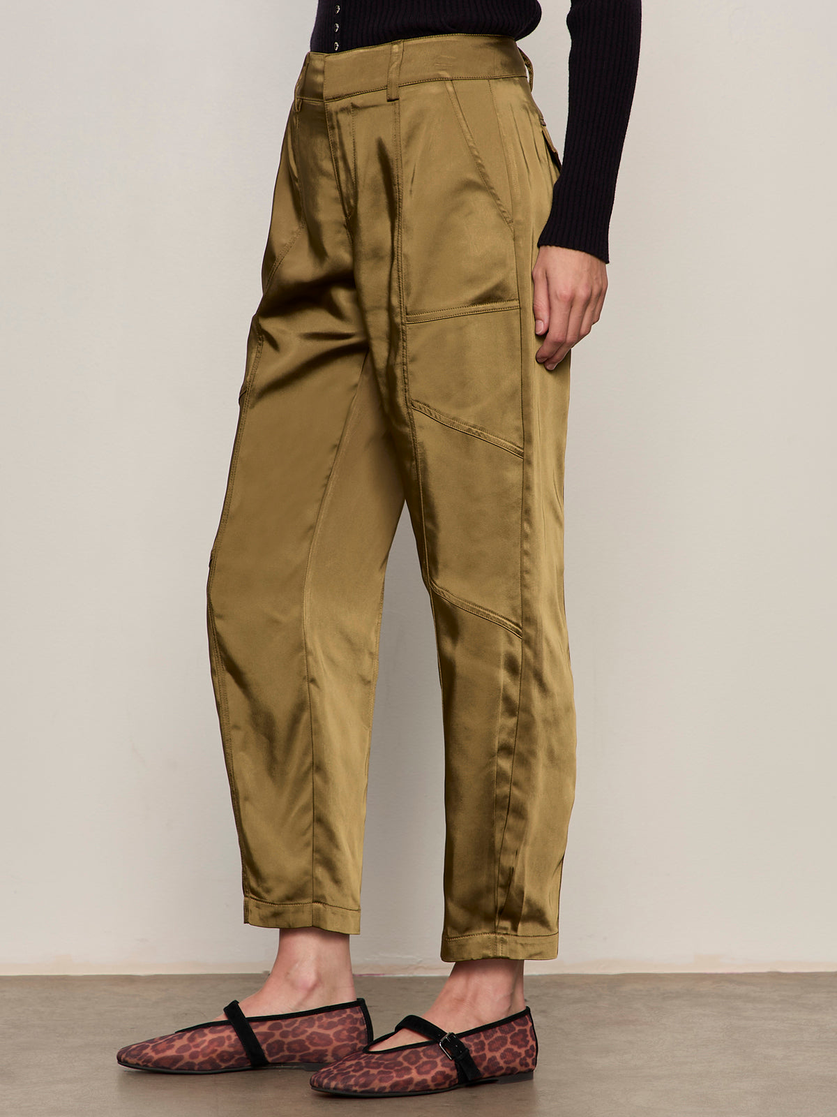 A person wearing Sanctuary Clothing's sahara satin tapered pant in dirty martini, a black ribbed long-sleeve top, and brown leopard print slip-on shoes stands against a neutral background.