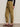 A person wearing Sanctuary Clothing's sahara satin tapered pant in dirty martini, a black ribbed long-sleeve top, and brown leopard print slip-on shoes stands against a neutral background.