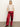 A woman stands against a plain light background, wearing Sanctuary Clothing’s satin track pant in crimson with white side stripes, a short-sleeved beige sequin top, and red heeled ankle boots. Her hands are in her pockets as she looks ahead.