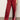 A person wears Sanctuary Clothing's satin track pant crimson—shiny red with white side stripes and a relaxed fit—paired with red heeled shoes. The photo, cropped at the torso, highlights the standout pants.