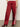 A person wears Sanctuary Clothing's satin track pant crimson—shiny red with white side stripes and a relaxed fit—paired with red heeled shoes. The photo, cropped at the torso, highlights the standout pants.
