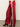 A person wears Sanctuary Clothing’s satin track pant in crimson, featuring a white side stripe and wide-leg fit, paired with maroon heeled shoes, standing on a grey floor against a plain light background.