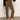 A person stands indoors in Sanctuary Clothing’s Fairway Legging in Dirty Martini, paired with a black sweater and black pointed flats. The image displays the lower half of the body against a plain background.