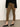 A person wears Sanctuary Clothing’s fairway legging dirty martini, a black long-sleeve top, and black flats while standing on a concrete floor against a light wall. The photo is cropped at the torso and ankles.
