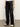 A person wears Sanctuary Clothing's coated twill track pant in black with white side stripes, a white T-shirt, and white sneakers, standing on a concrete floor against a plain light background.