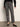A person stands against a plain wall wearing Sanctuary Clothing’s 90s straight legging burnt olive plaid petites, paired with a black sweater and black ballet flats. Their head is out of frame.