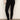 A person wears Sanctuary Clothing’s 90s Straight Legging in black, a light beige sweater, and black ballet flats, standing against a plain light wall with one hand on their hip.