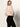 A woman with long blonde hair wears a light pink sweater and Sanctuary Clothing's 90s straight legging black pants, standing against a plain light background and looking back over her shoulder.