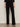 A person stands against a plain wall wearing Sanctuary Clothing’s marine ponte pant in black with black open-toe heels. Their arms are relaxed by their sides, and only their body from the shoulders down is visible.