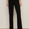 A person stands against a plain wall wearing Sanctuary Clothing’s marine ponte pant in black with black open-toe heels. Their arms are relaxed by their sides, and only their body from the shoulders down is visible.