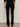 A person faces away from the camera wearing Sanctuary Clothing's velveteen brook bootcut pant in black petites and black high-heeled shoes, arms relaxed at their sides against a neutral background.