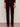 A person stands against a light background, wearing Sanctuary Clothing's velveteen brook bootcut pant in dark crimson petites, styled with black boots and a matching burgundy top; image is cropped from shoulders down.