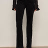 Wearing Sanctuary Clothing's velveteen brook bootcut pant in black with a black, flared-cuff long-sleeve top and black ankle boots, the person stands against a plain light wall, shown from shoulders to feet.