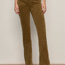 A person wearing Sanctuary Clothing's velveteen brook bootcut pant in dirty martini, paired with black heeled boots, stands against a light wall. Their upper body is mostly out of frame.