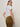 A person with straight, light brown hair wears a white t-shirt and Sanctuary Clothing's velveteen brook bootcut pant in dirty martini, standing sideways and looking over their shoulder against a plain light background.