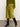 A person wearing a green buttoned sweater, Sanctuary Clothing's everyday midi skirt in martini olive, and black knee-high heeled boots stands on a gray floor against a plain off-white wall.