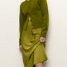 A person wearing a moss green cardigan and the Sanctuary Clothing everyday midi skirt in martini olive poses against a white background, partially lifting the skirt, with their face partly out of frame.