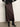 A person wearing the Sanctuary Clothing everyday maxi skirt semi sweet, paired with black pointed-toe heeled boots and a black sweater with white sleeve patterns, stands on a smooth gray floor against a light background.