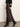 A person stands against a plain background wearing Sanctuary Clothing's everyday maxi skirt semi sweet in brown satin, paired with a black sweater featuring a white geometric sleeve pattern and black pointed-toe heeled boots.