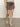 A person wearing the camden skirt french kitty by Sanctuary Clothing and light beige knee-high suede boots stands on a concrete floor against a plain white wall.