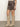A person wearing the Sanctuary Clothing camden skirt french kitty, a leopard print mini skirt, with light beige knee-high suede boots, stands on a concrete floor against a plain light-colored wall.