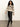 Woman wearing a patterned sweater and black pants against a plain background