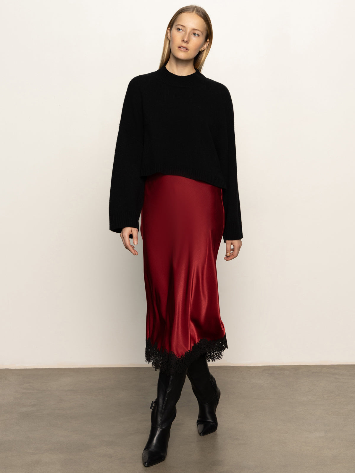 Woman wearing a black top and red skirt with black boots against a white background