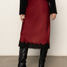 Red skirt with black lace trim worn with black knee-high boots on a neutral background