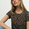 A woman with long blonde hair wears the Sanctuary Clothing "the perfect tee french kitty" t-shirt and blue jeans, accessorized with a gold necklace, sitting against a plain light background and looking confidently at the camera.