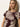 A woman with long blonde hair wears the Sanctuary Clothing "the perfect tee mesa palm," a maroon and beige T-shirt with a bold leaf pattern. She stands against a plain light background, looking slightly to the side with a neutral expression.