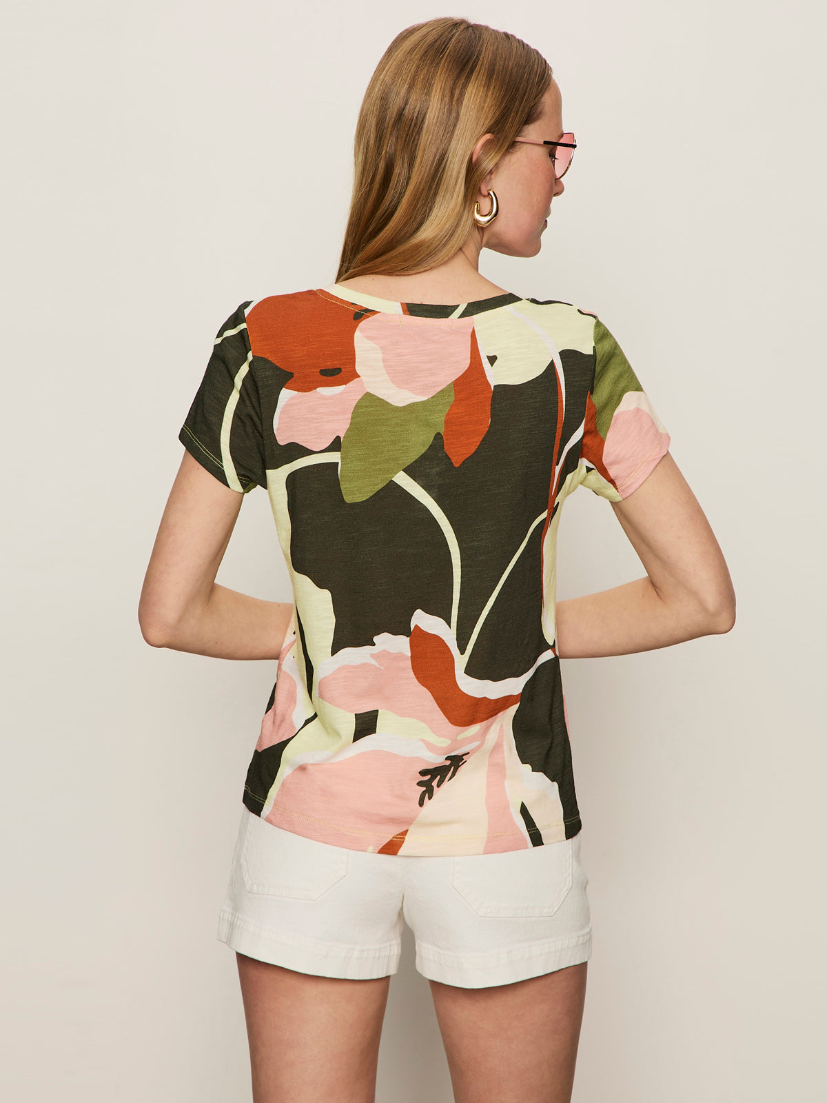 A woman with long blonde hair and hoop earrings wears Sanctuary Clothing's "the perfect tee reef vibes" t-shirt and white shorts, standing with her back to the camera against a plain background.