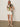 A woman wearing Sanctuary Clothing’s the perfect tee reef vibes, pink-tinted sunglasses, white shorts, and beige woven slip-on shoes stands with one hand in her pocket against a plain background.