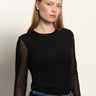 A person with long, straight blond hair wears the Sanctuary Clothing long sleeveperfect mesh tee in black, styled with blue jeans and a black belt, standing against a neutral background.