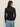 A woman with long brown hair models the Sanctuary Clothing dreamgirl lace button up black, paired with light blue jeans and gold hoop earrings, standing with her back to the camera against a plain light background.