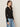 A woman stands in profile against a plain background, wearing the Sanctuary Clothing dreamgirl lace button up black shirt with a collar and light blue jeans. She has loose brown hair and small hoop earrings.